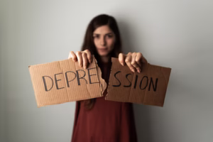 Latin young woman recovered from depression Acceptance Path Counseling A woman tearing a cardboard sign that says DEPRESSION in half symbolizing the power to break cycles and overcome the hereditary risks associated with the question Is depression genetic