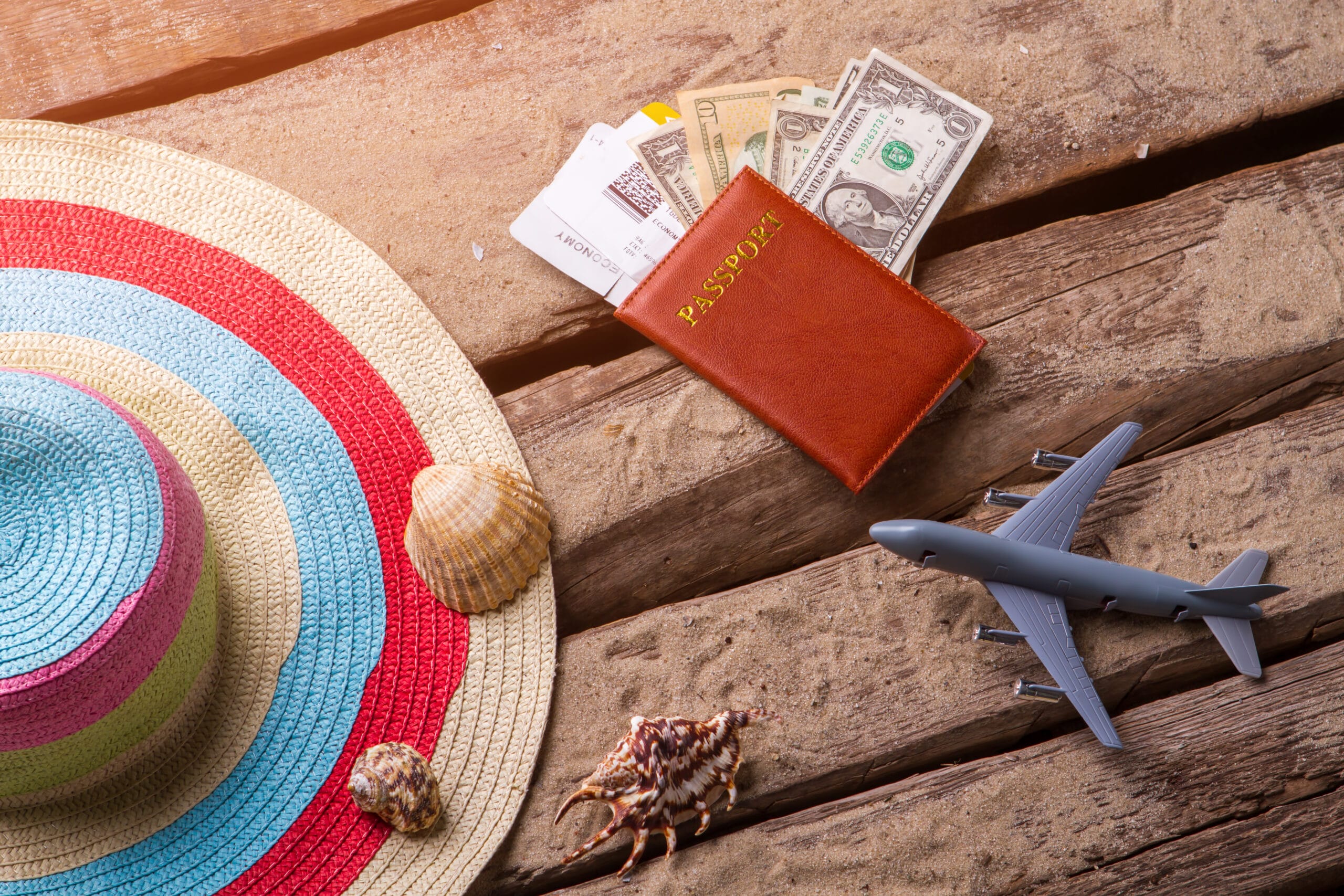 Beach hat and passport Acceptance Path Counseling A passport plane tickets and money on a wooden surface illustrating the hidden costs of escapism and why travel is good for your mental health only when aligned with values