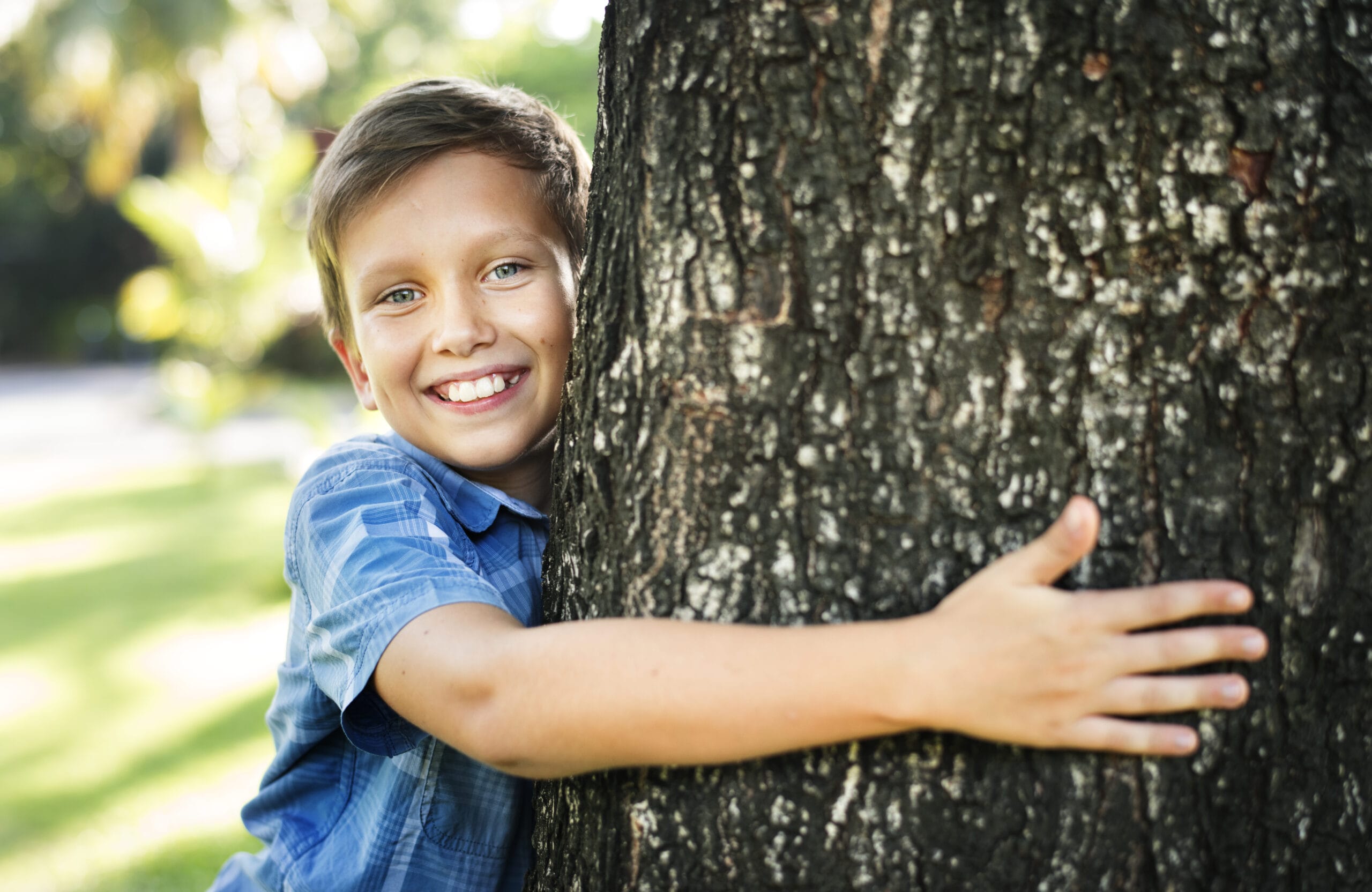 Boy hugging a big tree in the park Acceptance Path Counseling Happy child reconnecting with nature in The Woodlands after receiving local ADHD therapy near Rayford
