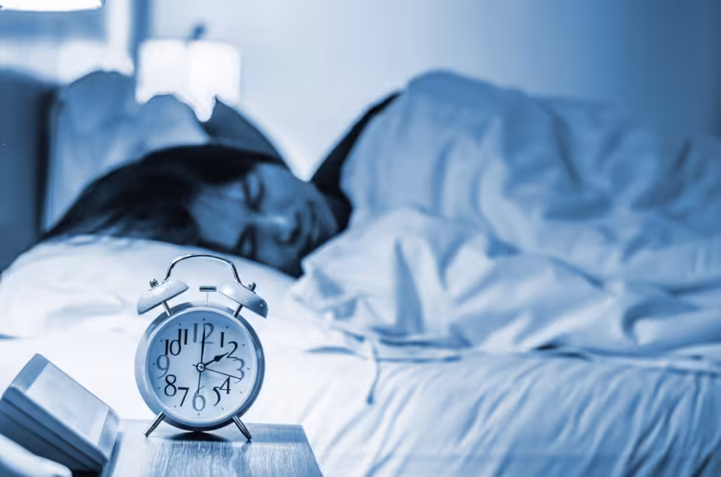 A restless individual struggling with sleep, lying in bed alongside a visible alarm clock, illustrating the difficulty of Breaking the Insomnia Cycle in The Woodlands