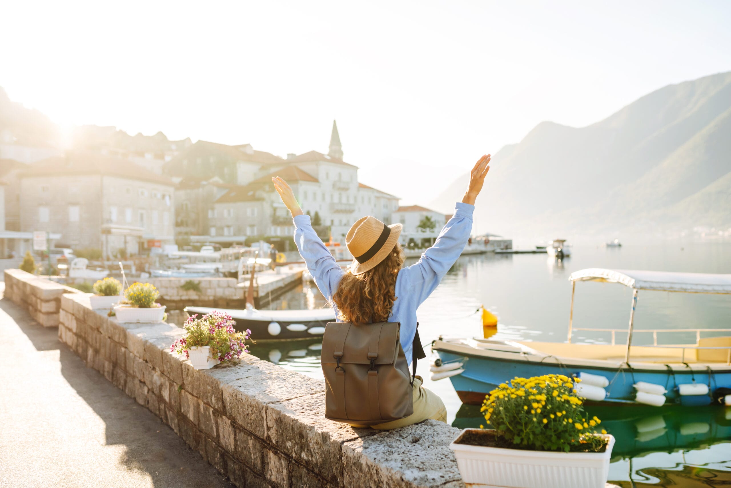 Tourist woman admiring view of colorful view of city Back view Europe travel Lifestyle nature Acceptance Path Counseling A woman with a backpack raising her arms in joy by a harbor illustrating the psychological benefits of strategic travel and why travel is good for your mental health
