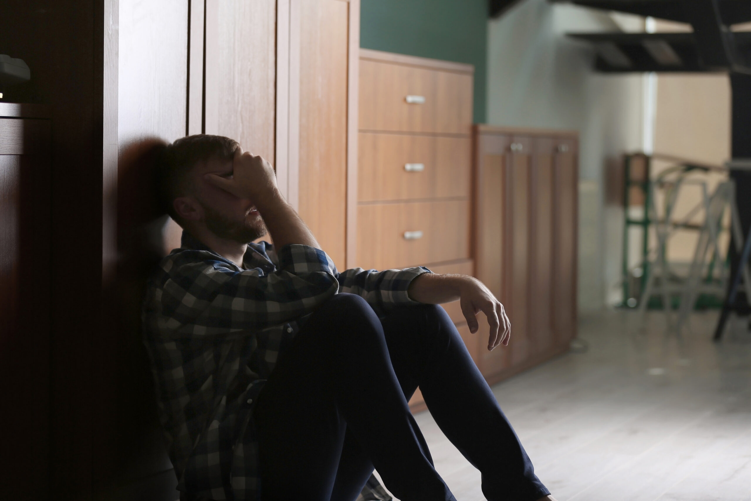 An exhausted man sitting on the floor with his hand over his face conveying the biological drain of ADHD and depression for adults in The Woodlands