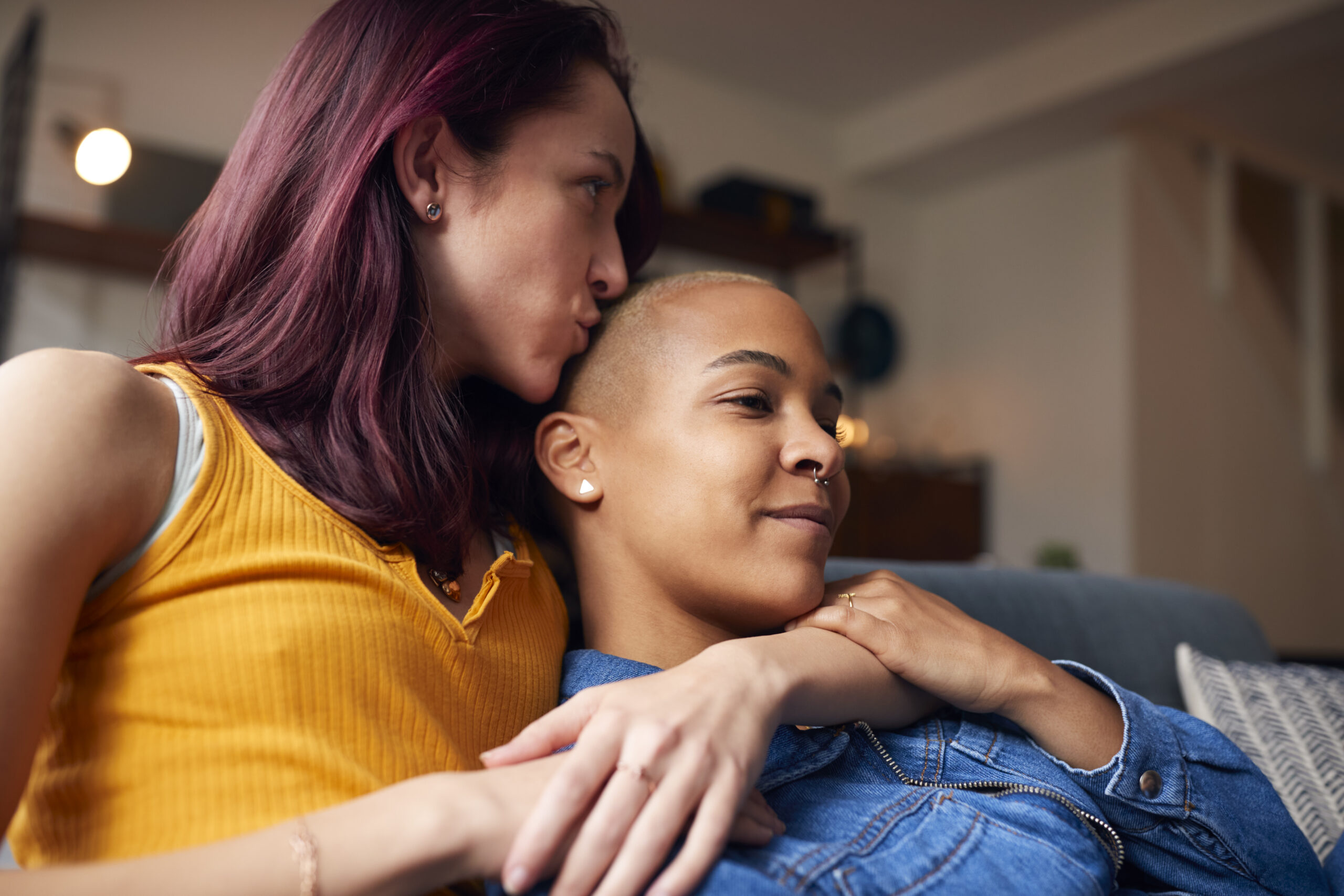 A close up of a woman in a yellow top embracing and kissing the forehead of her partner showing a physical and emotional act that demonstrates how to support someone with depression