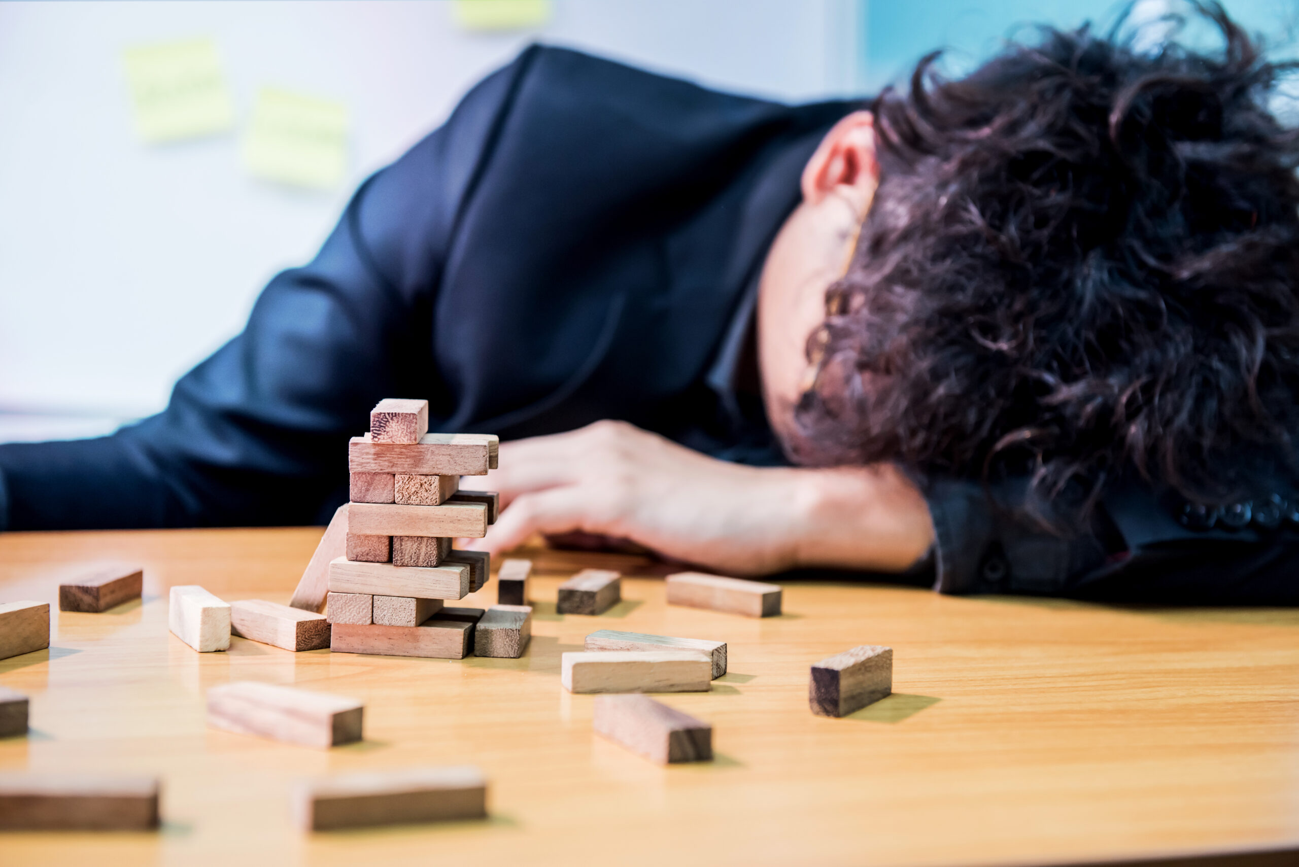 A stressed man slumps his head onto a desk next to wooden blocks The image captures the deep mental burnout that comes with managing severe contamination phobia