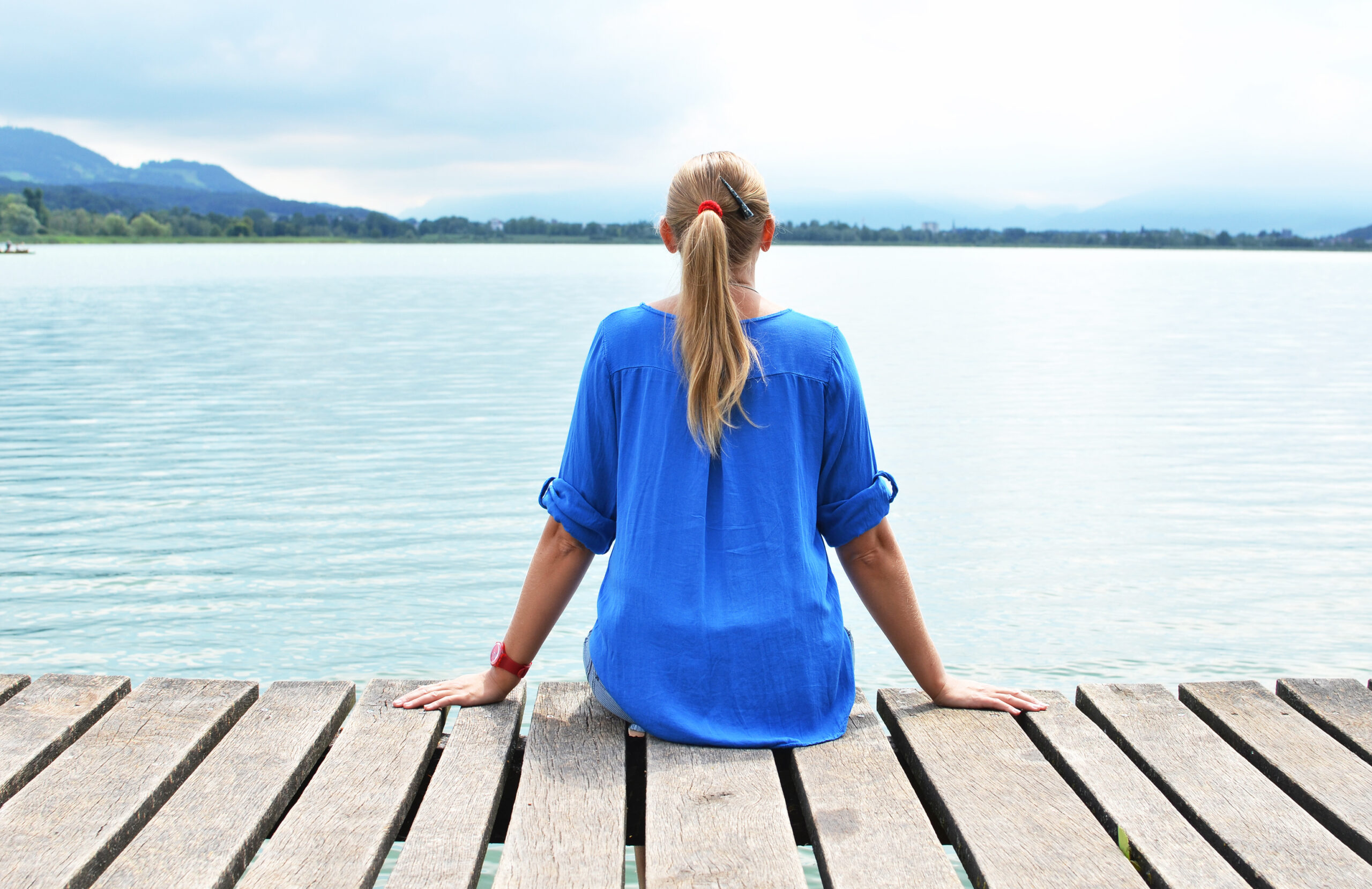 A woman sitting alone at the edge of a wooden pier overlooking calm water illustrating the quiet personal moments of reflection before seeking depression support