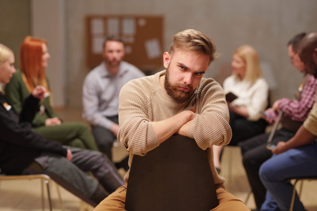 A professional in Greenwood Forest sitting quietly withdrawn in a group session — reflecting the shame-driven isolation that keeps harm OCD examples unspoken for years before reaching Acceptance Path Counseling