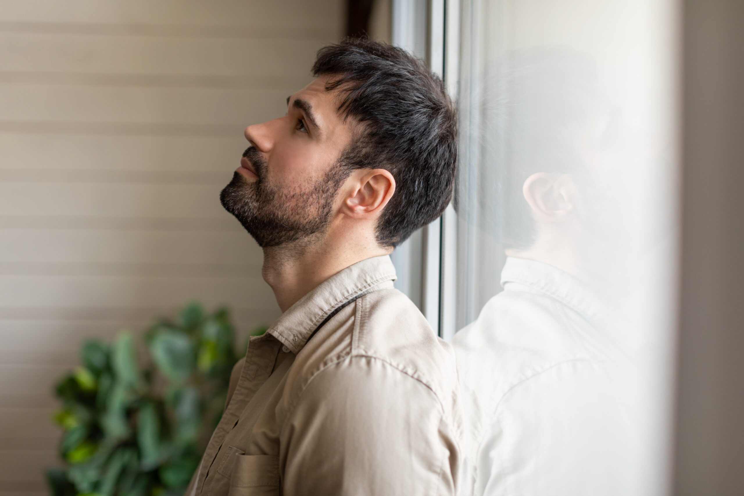 A professional in Greenwood Forest standing alone at a window lost in thought capturing the invisible mental exhaustion of unmedicated OCD that Acceptance Path Counseling helps address