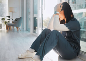 A healthcare professional in scrubs resting her head in her hands while sitting on the floor capturing the essential self care moments needed when overcoming depression