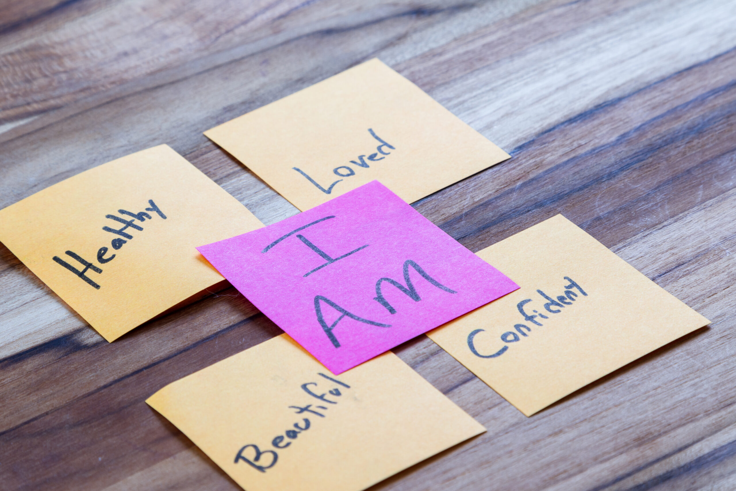 Colorful sticky notes arranged on a wooden table display positive self affirmations like I Am Loved and Healthy It provides a visual example of behavioral exercises and everyday coping mechanisms for depression