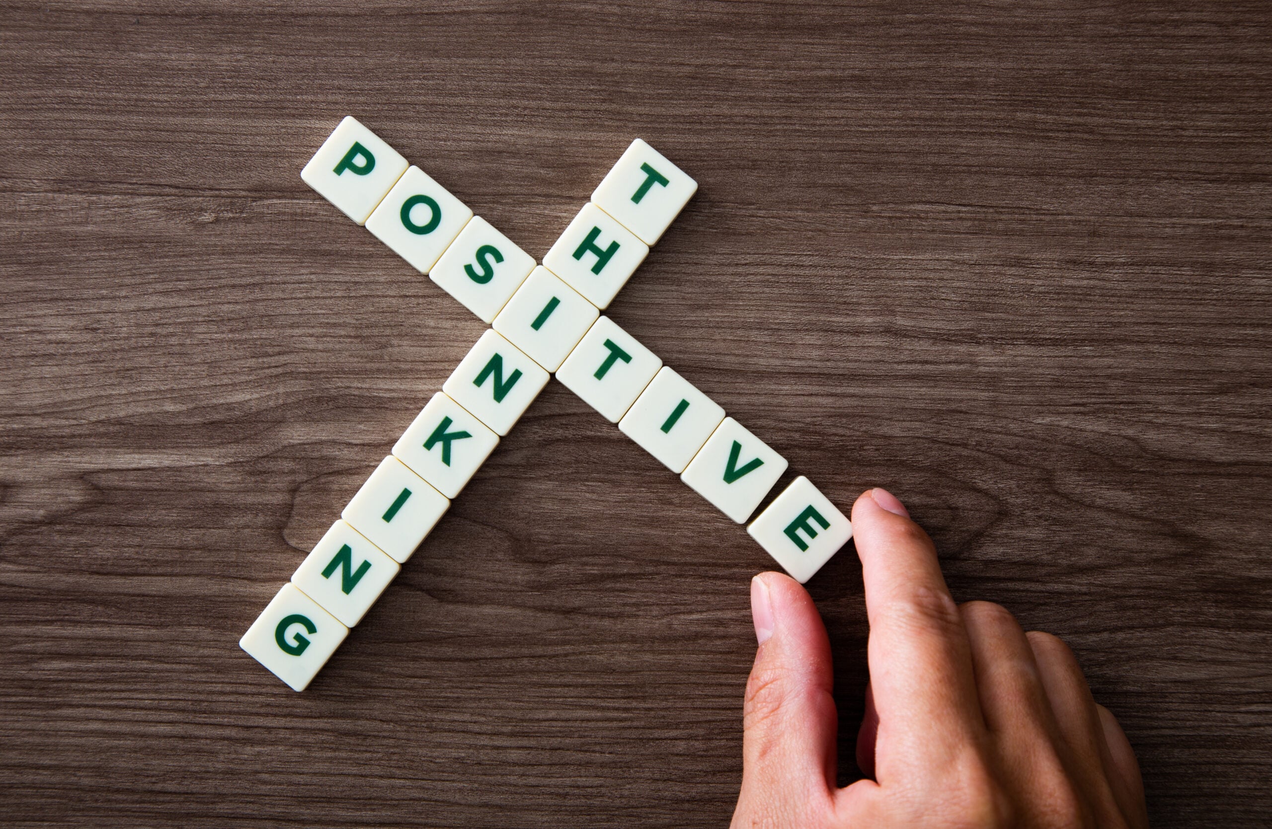 A hand arranging wooden letter tiles to form the words positive thinking highlighting the mental effort involved in managing early signs of depression
