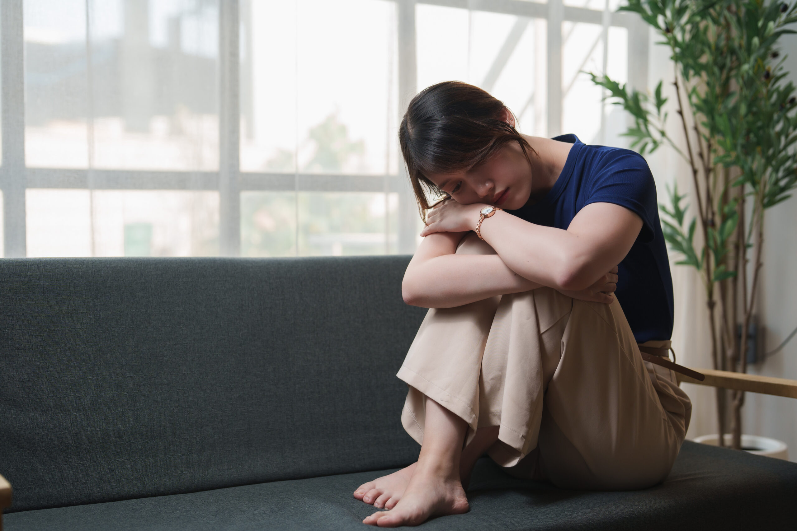 A woman sits on a dark couch with her knees tucked tightly to her chest in a home setting This visual represents the raw symptoms of executive dysfunction and underscores when to seek professional coping mechanisms for depression in The woodlands