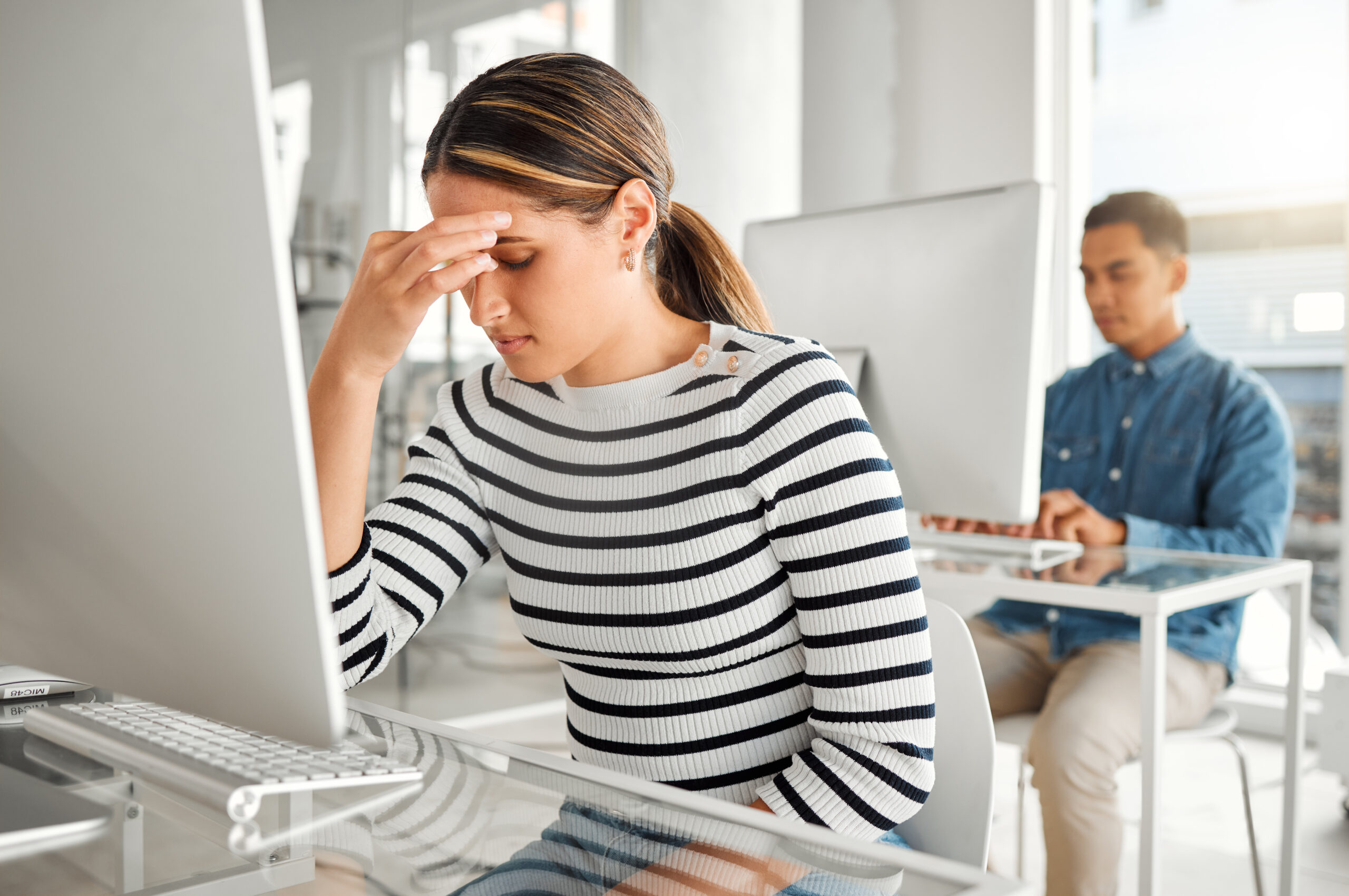 A stressed professional holds her head while sitting at a computer desk in a busy office It reflects the intense concentration needed to handle a workplace with adhd and ocd together