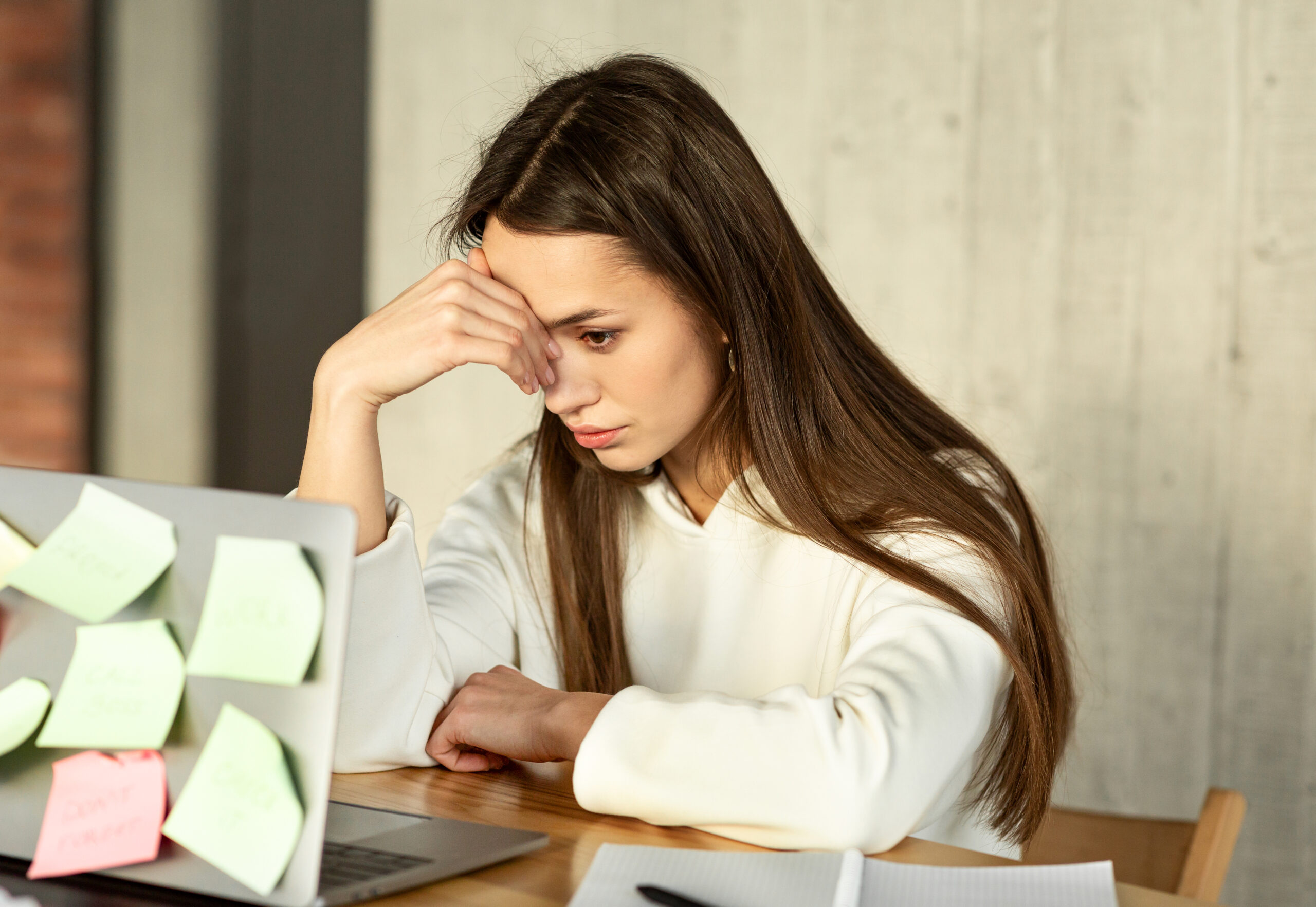 An exhausted individual leans over a laptop surrounded by a cluttered desk of scattered papers The chaotic setup illustrates the struggle of managing competing mental demands when living with adhd and ocd together