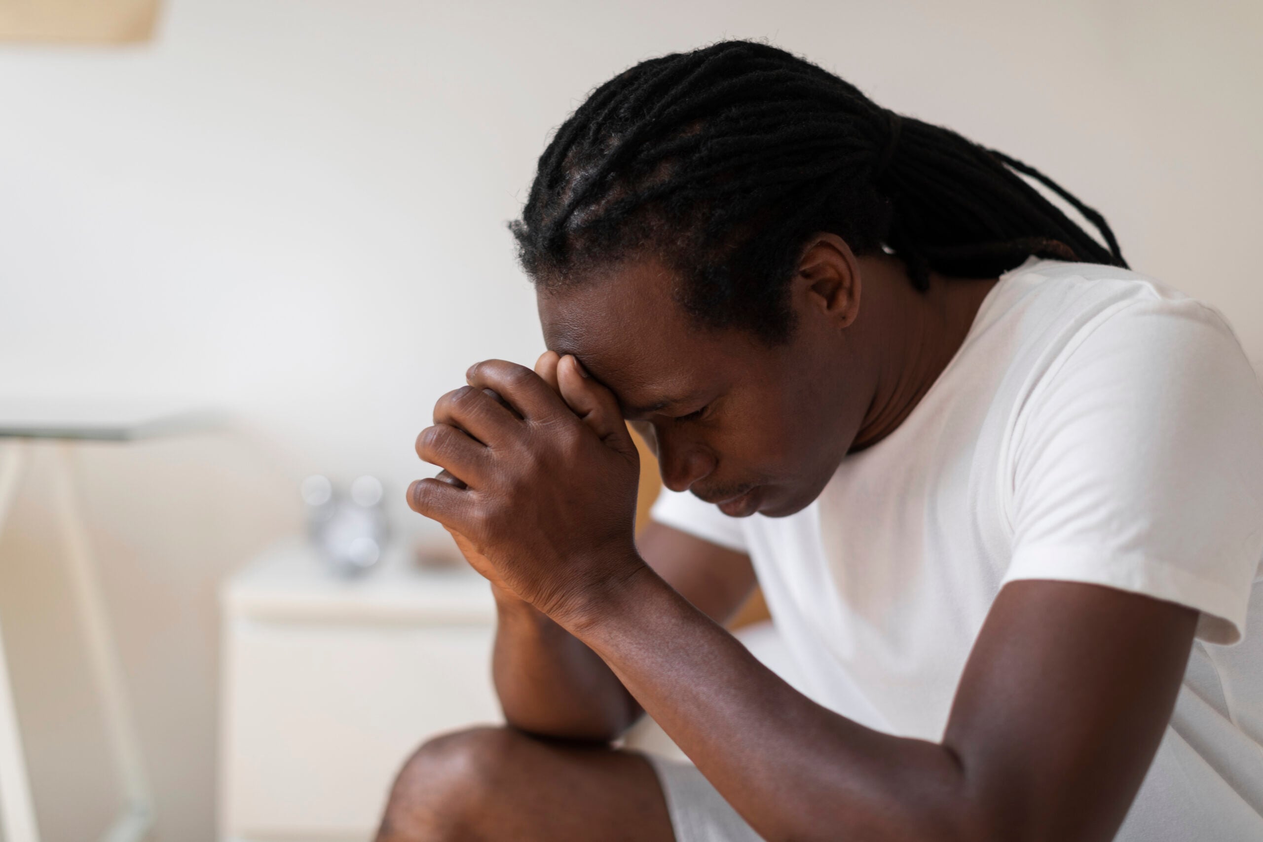 A man sitting on the edge of his bed with closed eyes and clasped hands reflecting the deep emotional fatigue and internal struggle associated with signs of depression