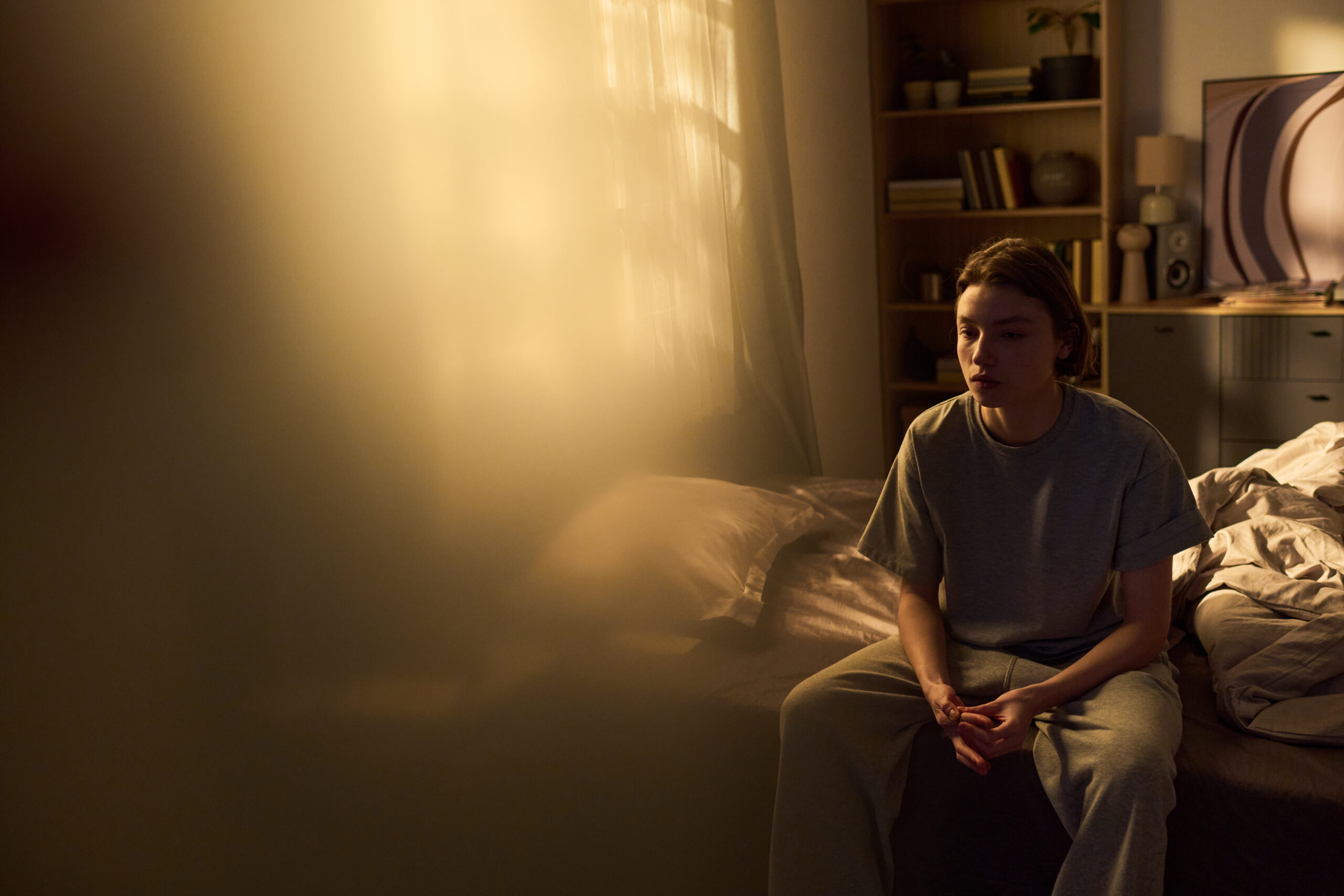 A person in Kohrville sitting alone on the edge of a bed in warm morning light with hands clasped  mid examination of guilt that resolves for genuine conscience but returns relentlessly with moral scrupulosity OCD addressed at Acceptance Path Counseling