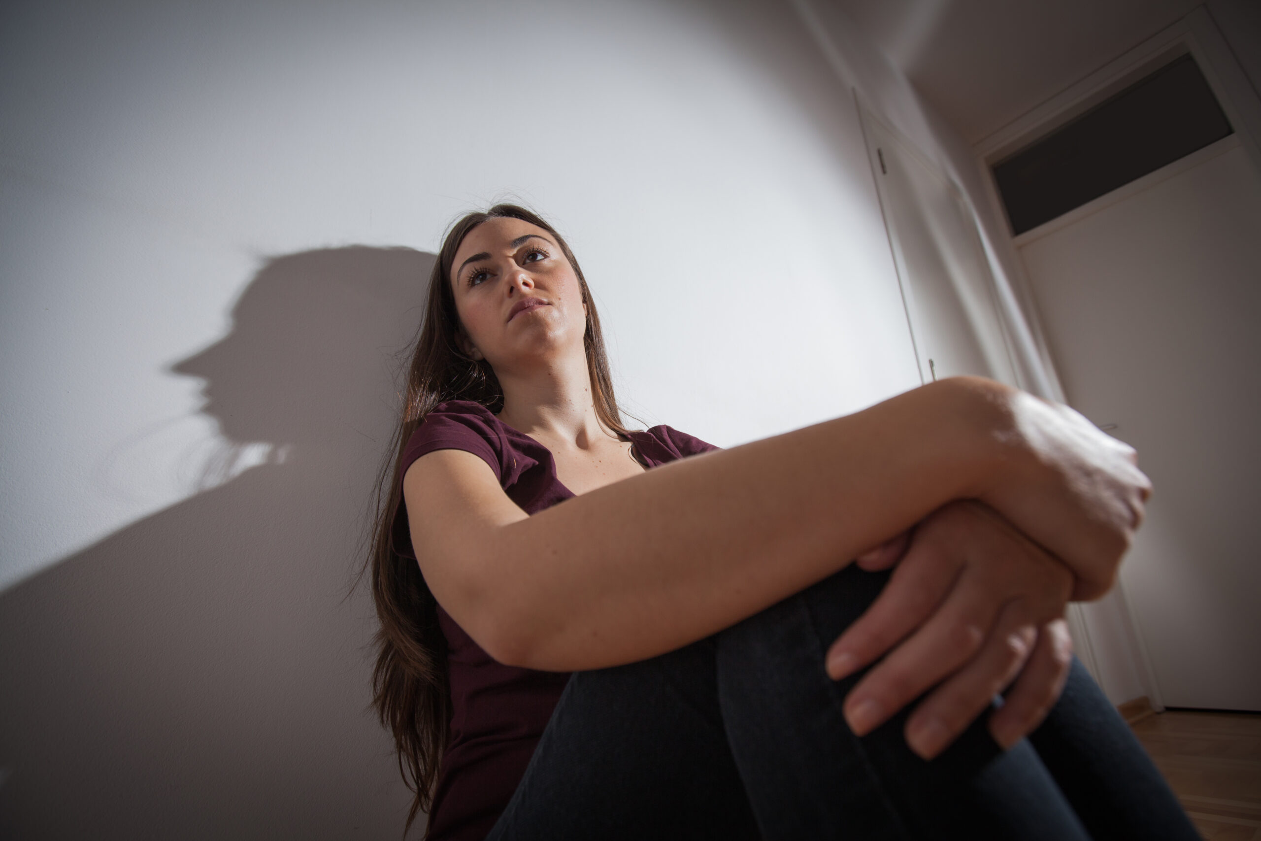 A woman sitting in a dimly lit room looking up toward a source of light symbolizing hope and the gradual mental shift toward overcoming depression