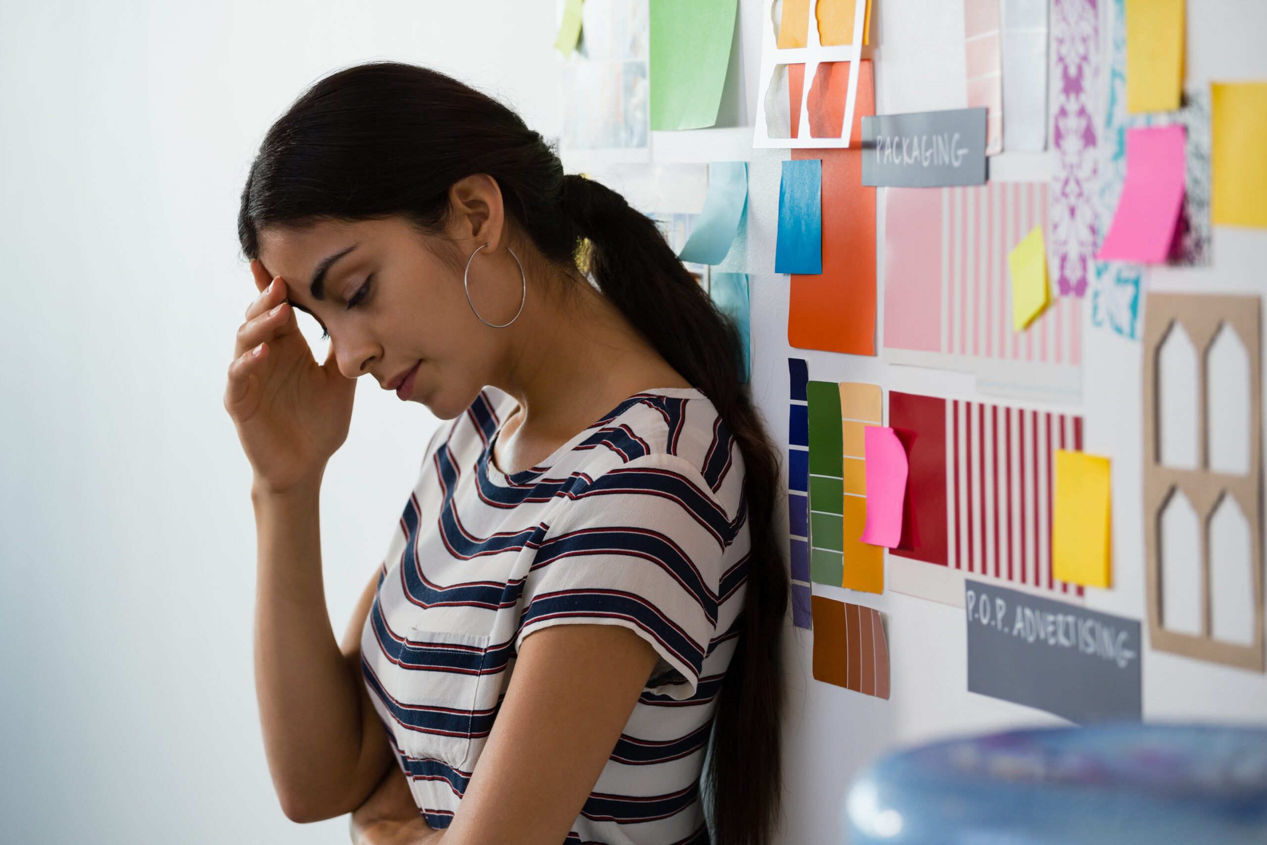A frustrated woman stands at a workspace covered in colorful notes with her hand on her forehead The scene captures the overwhelming mental exhaustion of navigating adhd and ocd together