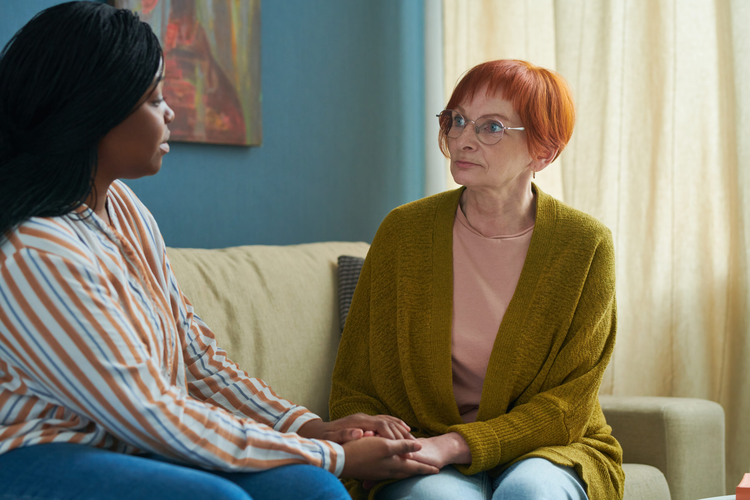 Two women sitting together on a comfortable sofa holding hands and making direct eye contact showing a dedicated one on one environment for depression support