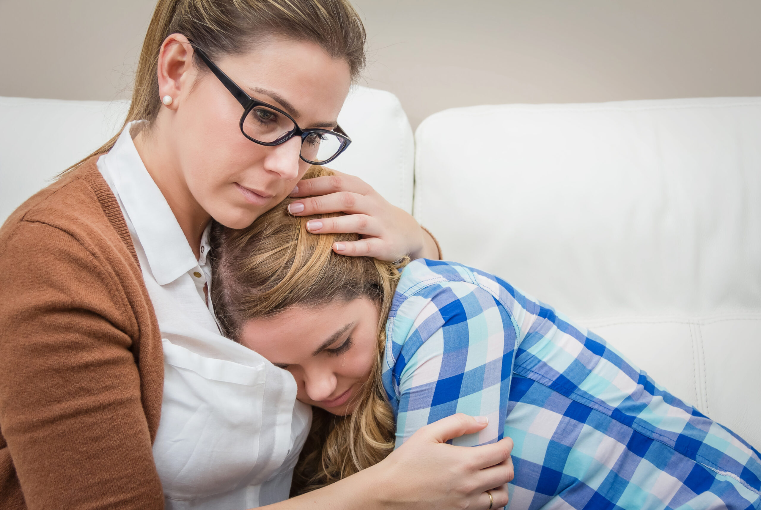 A supportive woman holding and comforting a sad young woman crying on a couch illustrating compassionate ways on how to support someone with depression during a crisis