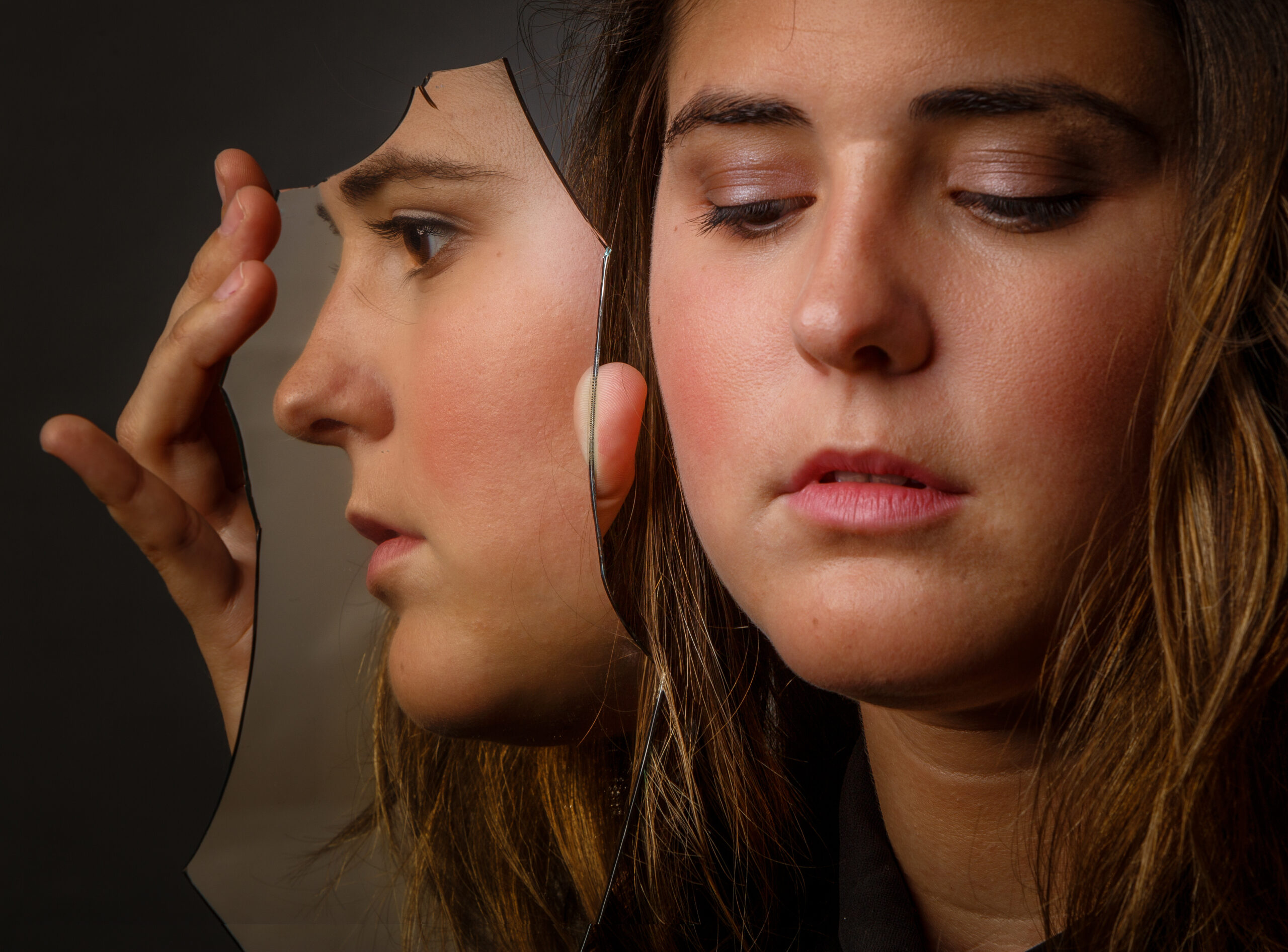 A woman in Kohrville holding a broken mirror to her face with eyes downcast  capturing the fractured self perception and relentless moral self examination of scrupulosity OCD addressed at Acceptance Path Counseling