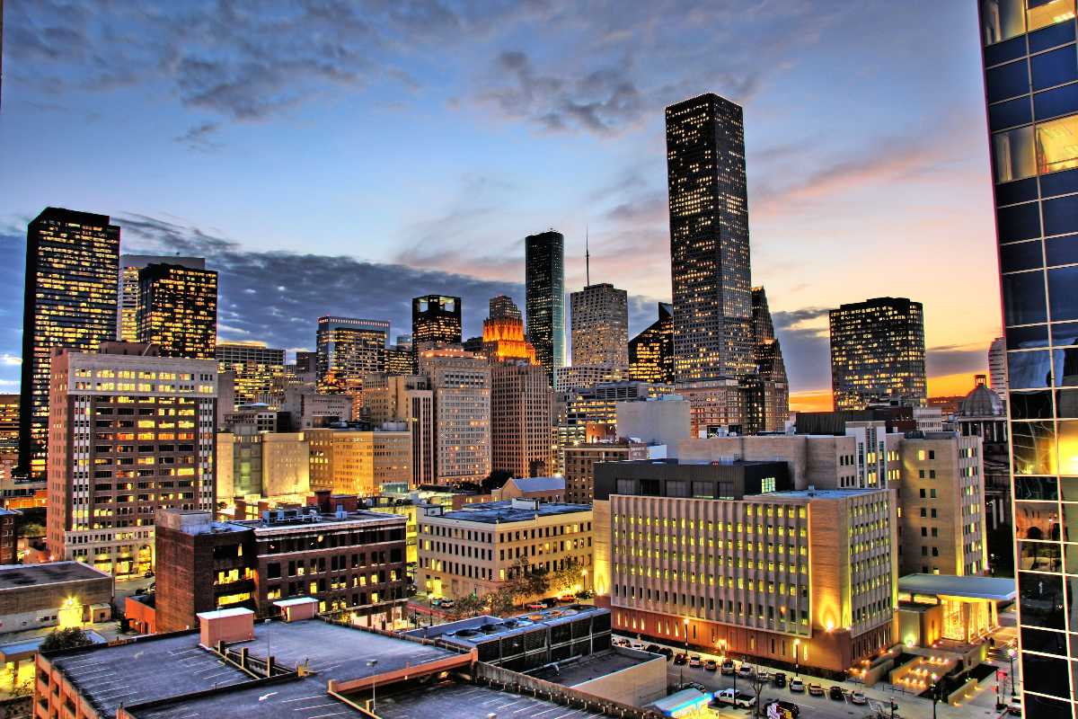City skyline at sunset with tall buildings and glowing windows over a dense urban foreground