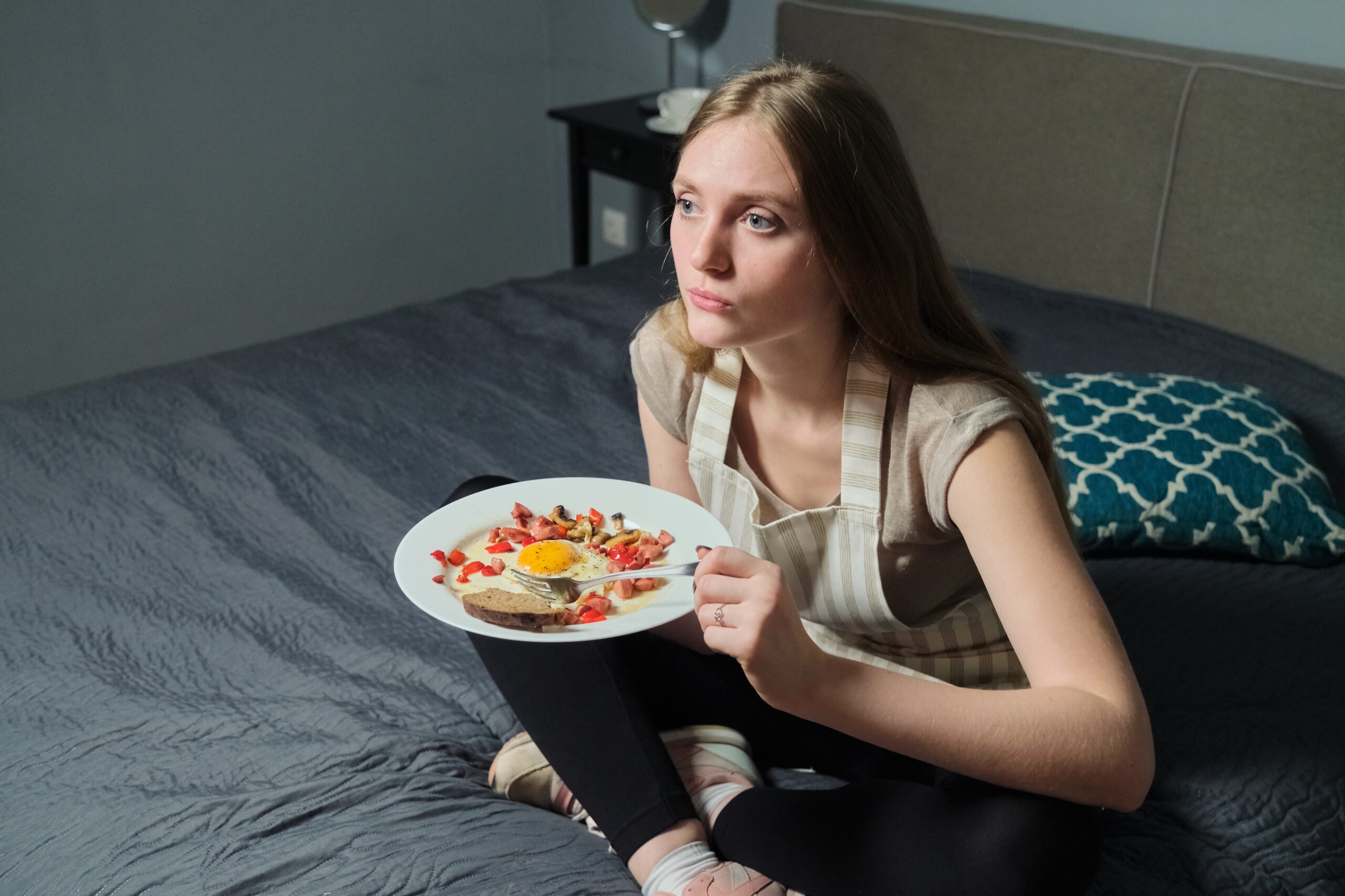 Girl sitting on bed with remote control watching TV and eating Acceptance Path Counseling Recovery process from an eating disorder involving therapy and healthy coping skills