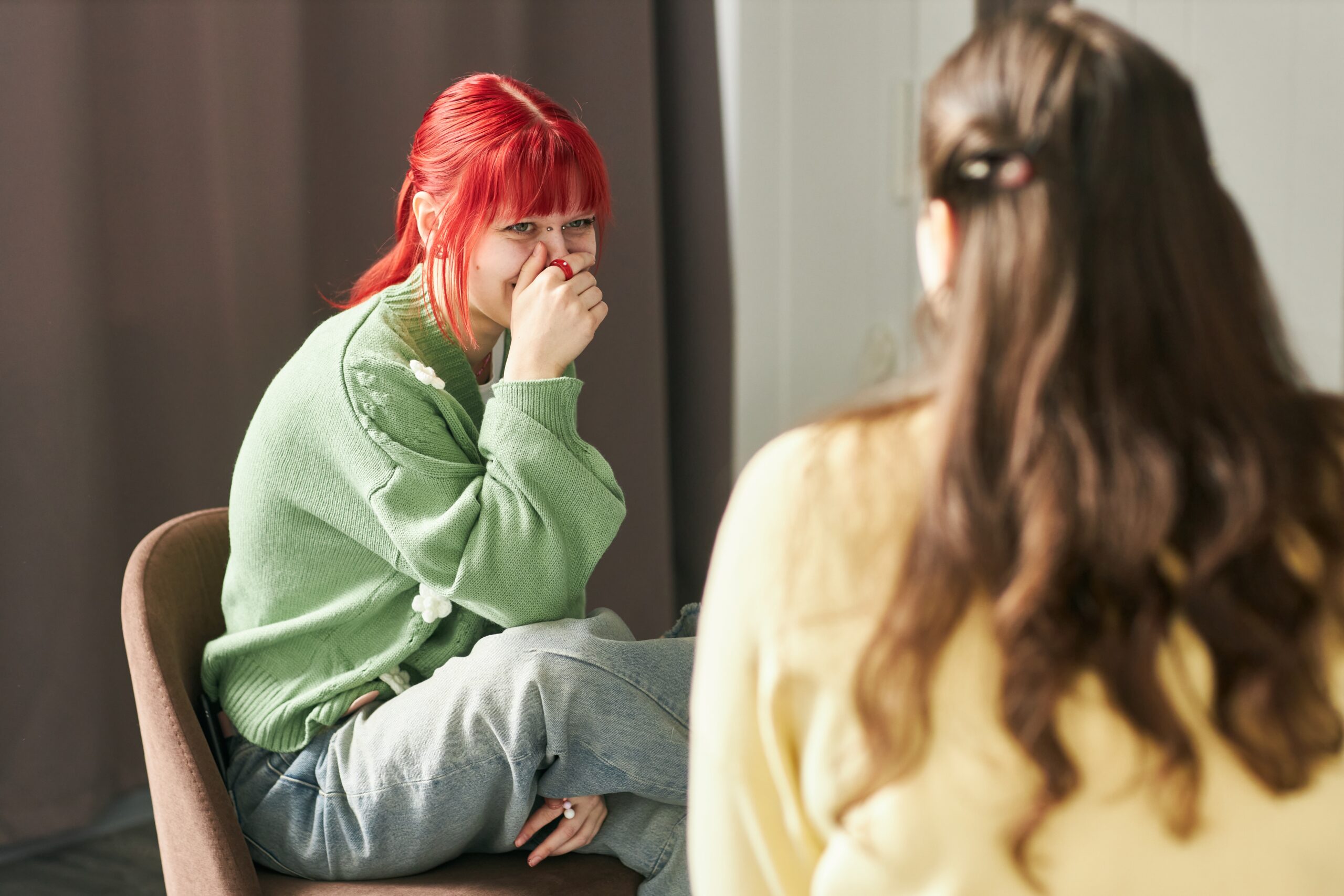 Smiling Woman with Red Hair Sitting on Chair Looking Away Acceptance Path Counseling Person reflecting on emotional changes linked to bipolar disorder symptoms