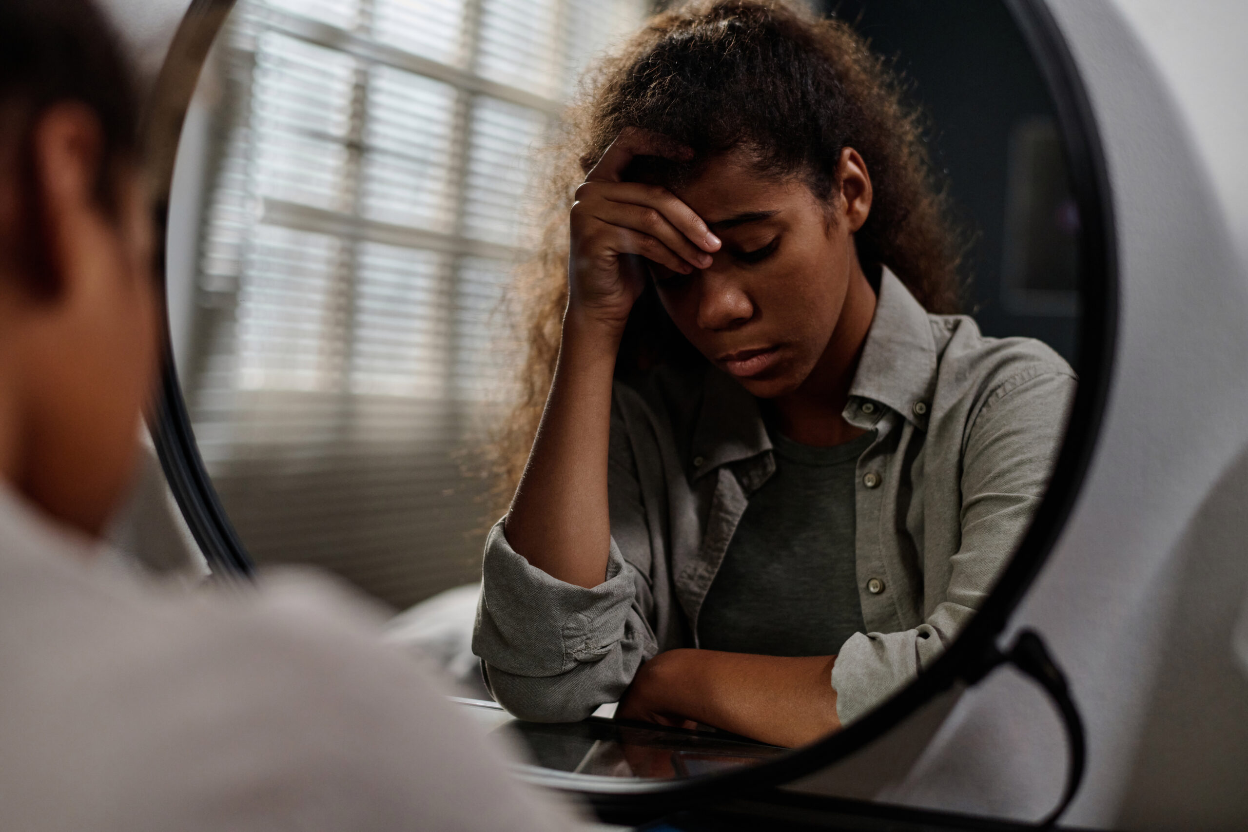 Offended teenage girl touching her forehead while sitting in front of mirror Acceptance Path Counseling Illustration representing emotional highs and lows in bipolar disorder