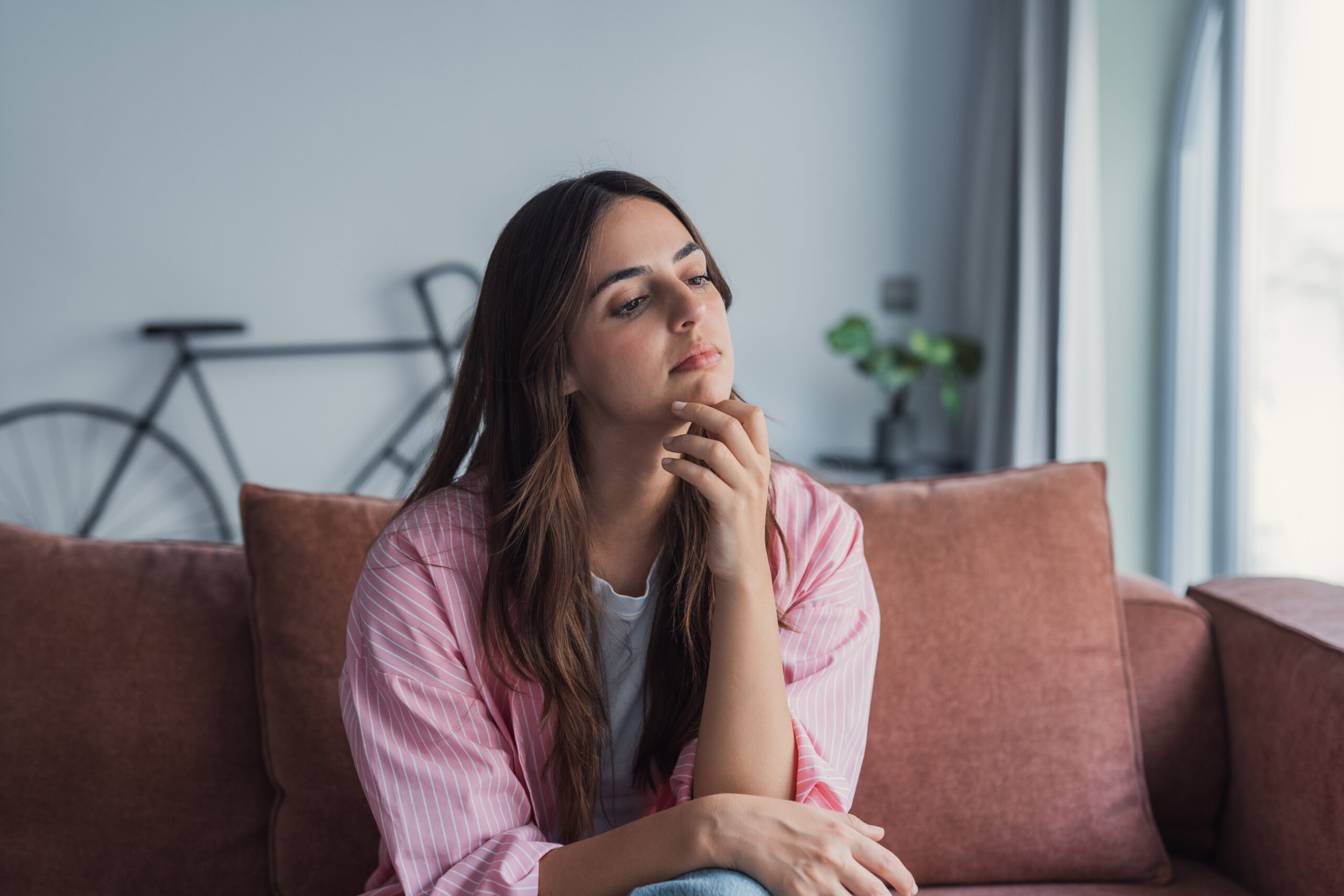 An upset young woman sits alone indoors reflecting on relations Acceptance Path Counseling Individual feeling overwhelmed by anxiety and overthinking during everyday life