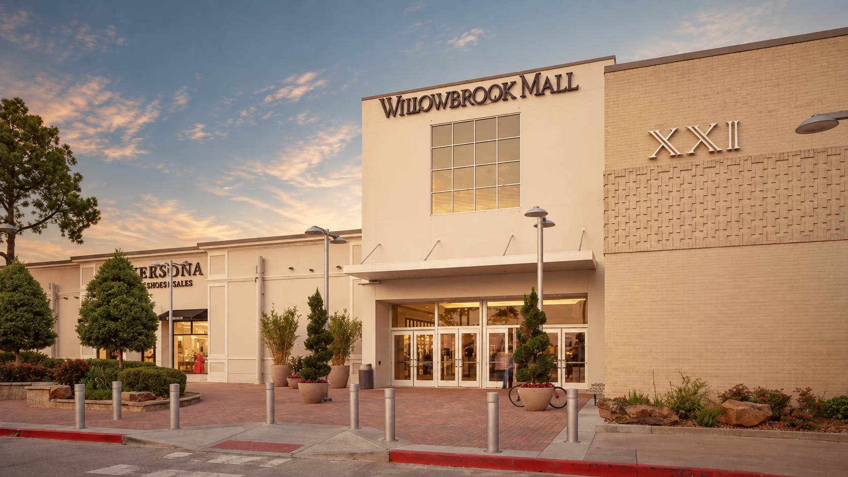 Front of Willowbrook Mall with a large glass windowed center entrance and the mall name Willowbrook Mall above set during sunset