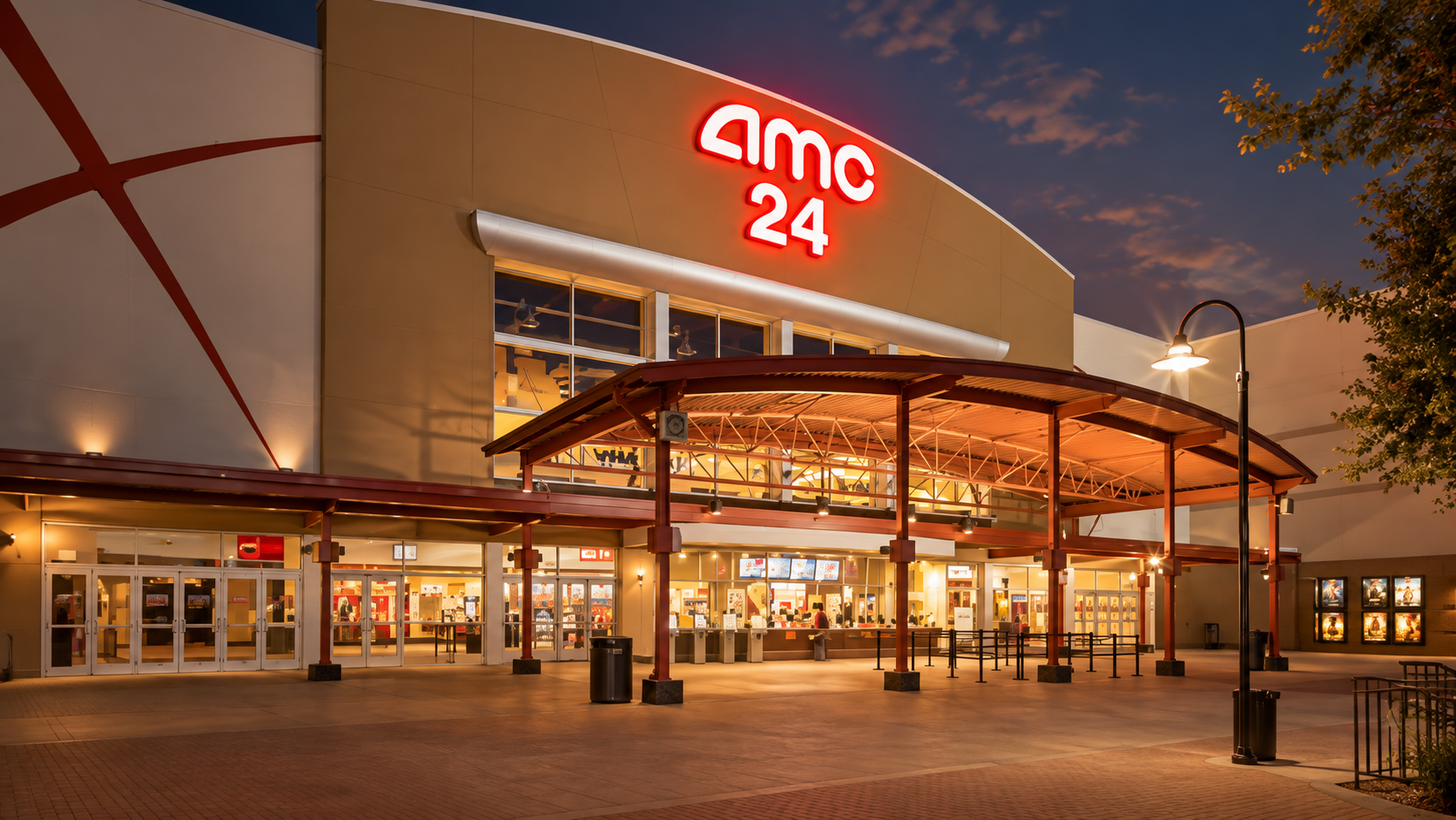 Exterior of an AMC 24 cinema at night with a glowing red sign glass doors and a curved wooden canopy over the entrance