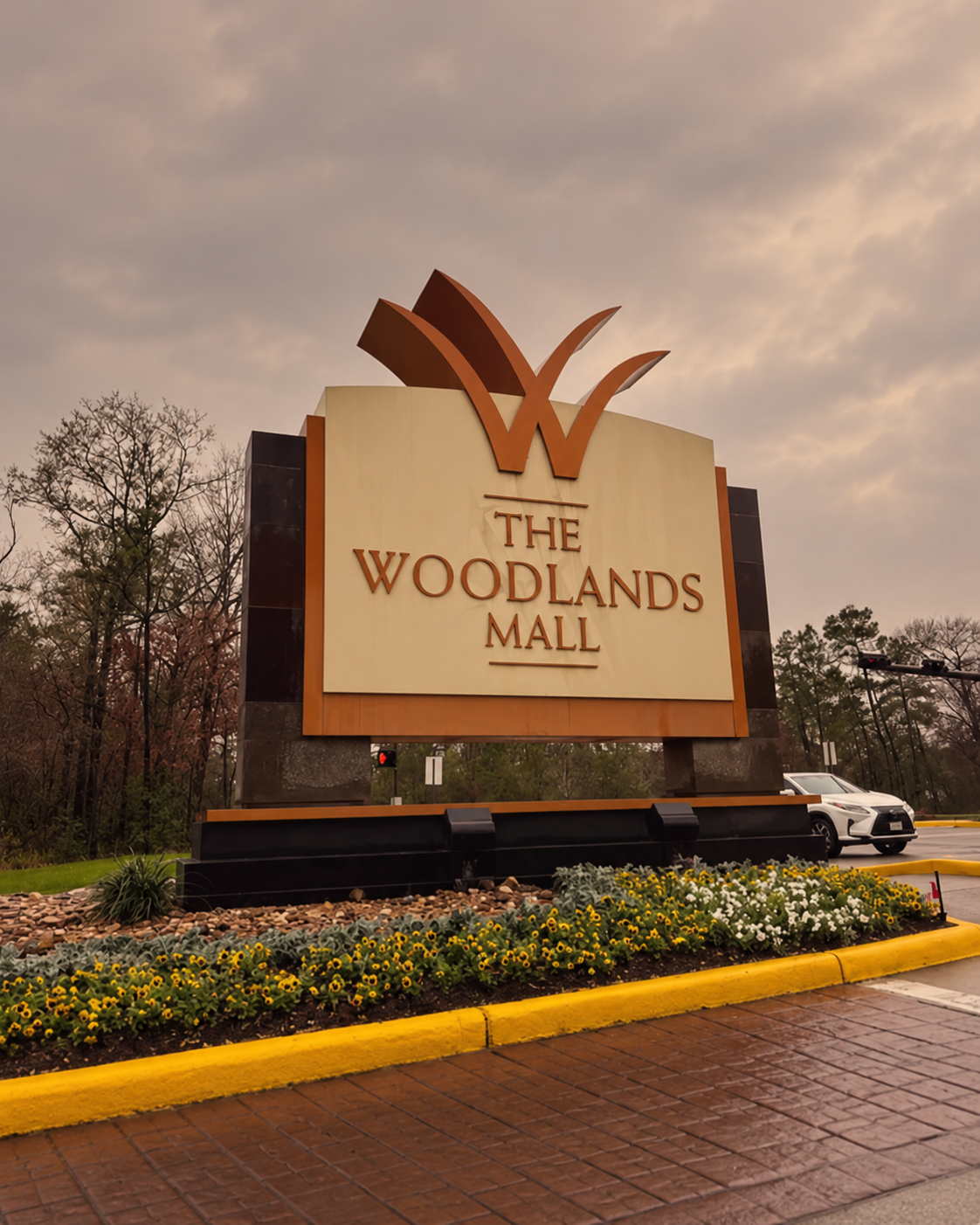 Front view of The Woodlands Mall sign with a large orange W logo and landscaping around it