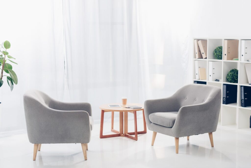 Two gray armchairs face each other beside a small table in a bright room