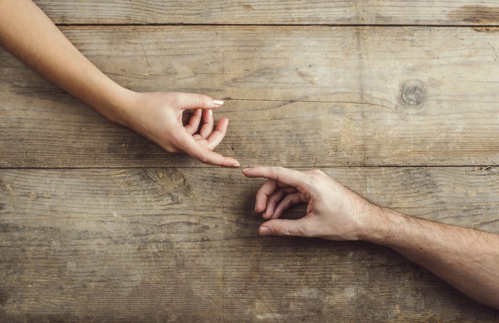 Two hands reach toward each other across a weathered wooden table