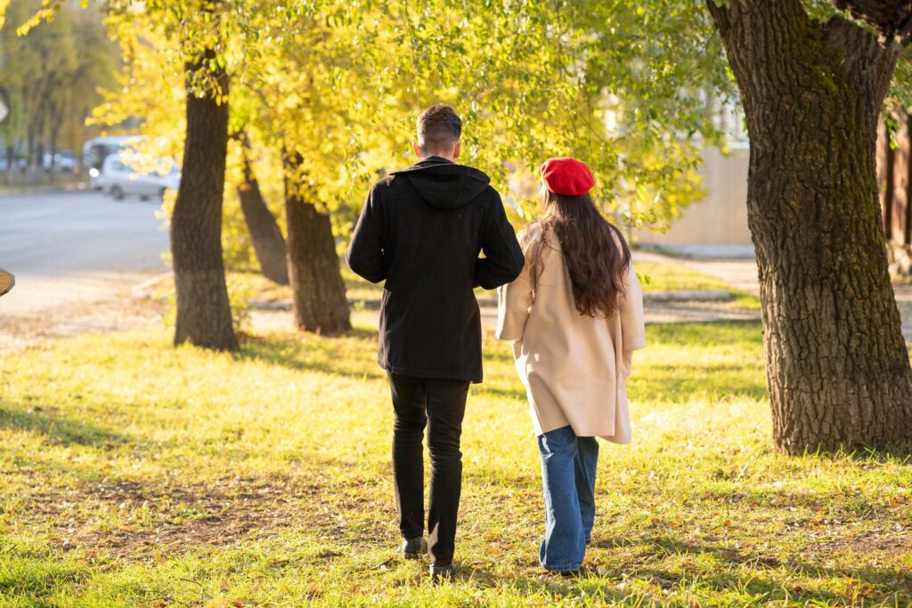 Two adults walk together across a grassy park under yellow autumn trees